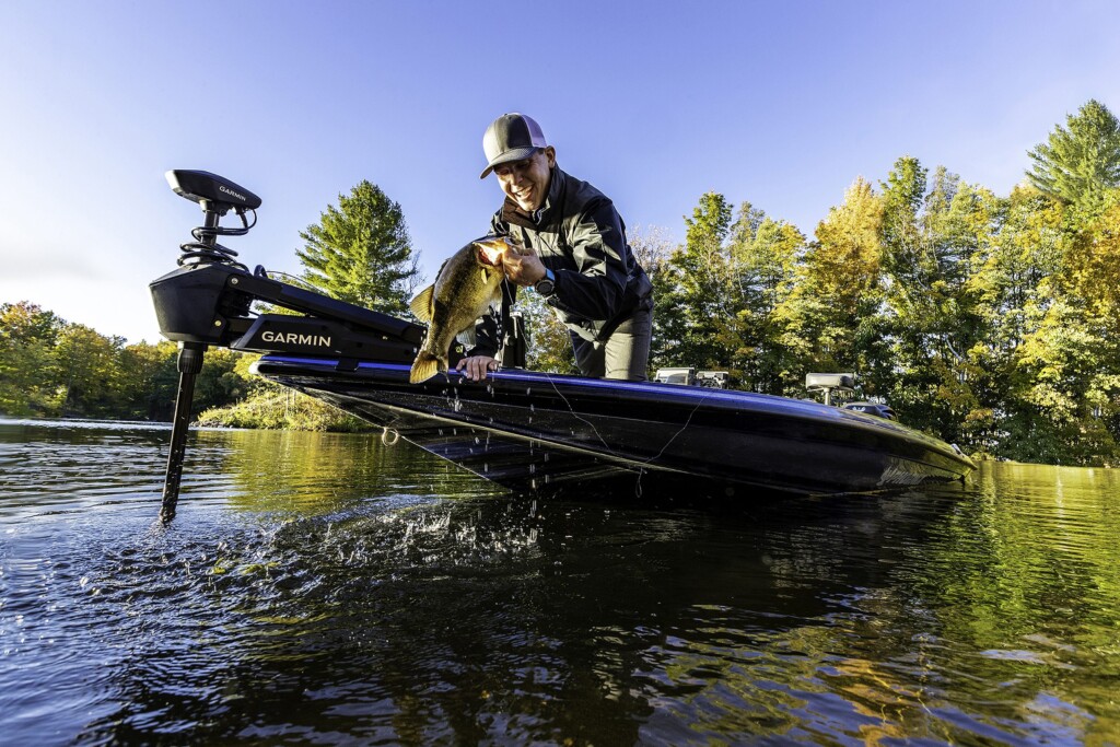 An angler holding a largemouth bass beside his electric trolling motor